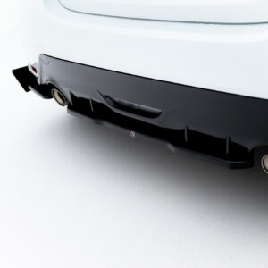 Close-up of a white car's rear bumper showing a black diffuser and a round exhaust tip visible on the right side.
