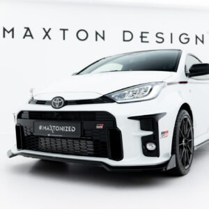 White Toyota sports car photographed from a low front-right angle in a bright showroom; background shows the brand 'MAIXTON DESIGN' (Maxton Design) sign and the car's grille and headlights are prominent. The license plate reads '#MAXTONIZED'.