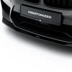 Close-up of a black car front with a centered license plate reading #MAXTONIZED and a honeycomb grille below it.