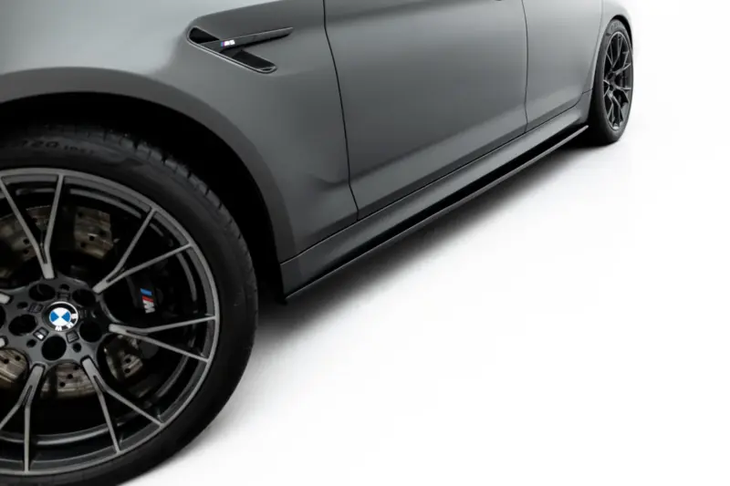 pol_po_Set-of-Splitters-V-1-BMW-M5-F90-23925_2webp - OPSHOLDERS Close-up of a gray BMW car's front-left side, featuring a large black alloy wheel, brake rotor, and a side vent with M badge