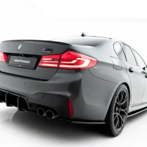 Rear three-quarter view of a gray BMW M5 Competition with a spoiler, illuminated taillights, and quad exhausts on a white backdrop (#MAXTONIZED).