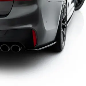 Close-up of the rear quarter panel of a dark gray sports car, showing its dual exhausts and rear bumper details.