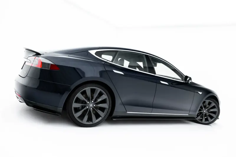 Rear-left side view of a dark blue Tesla Model S in a studio setting, highlighting the rear lights and aerodynamic bodywork.