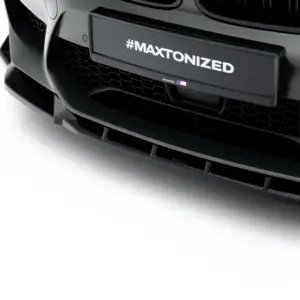 Close-up of a dark sports car front with a license plate reading '#MAXTONIZED' and a small M logo in the corner.