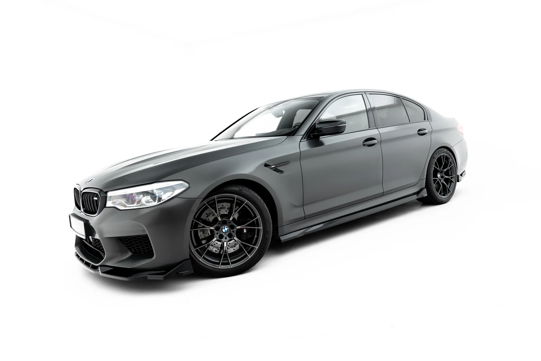 pol_po_Set-of-Splitters-V-2-BMW-M5-F90-23926_14webp - OPSHOLDERS Gray BMW sport sedan angled to show the front and side, featuring large black alloy wheels, against a white studio background.