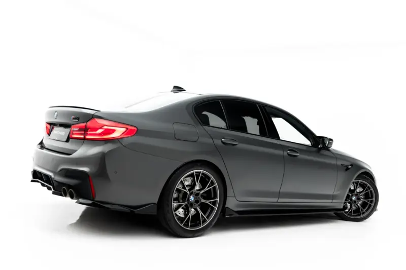 pol_po_Set-of-Splitters-V-2-BMW-M5-F90-23926_5webp - OPSHOLDERS Rear three-quarter view of a gray BMW M4 with red taillights and large alloy wheels, studio backdrop