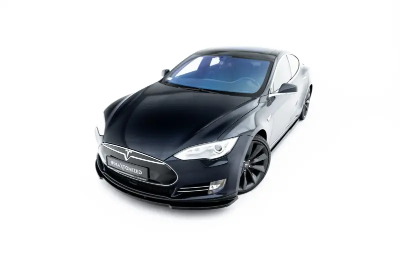 Front three-quarter view of a dark Tesla electric car against a white background, showing its sleek hood and distinctive front grille emblem.