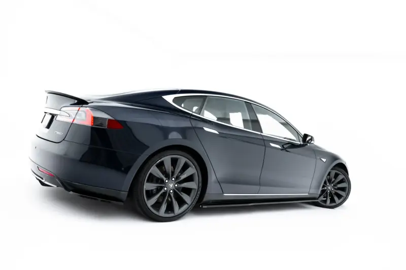Partial side view of a dark gray Tesla Model S showing rear quarter, door, and large wheels against a white background.