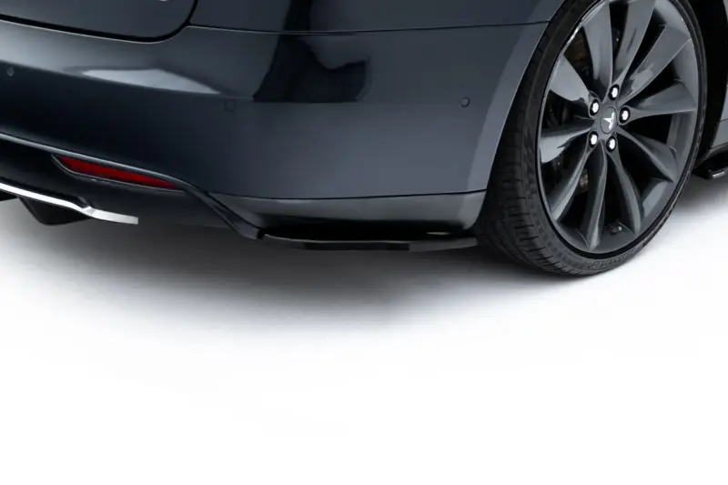 Close-up of a dark gray car's rear bumper and right rear wheel with a multi-spoke alloy rim visible.