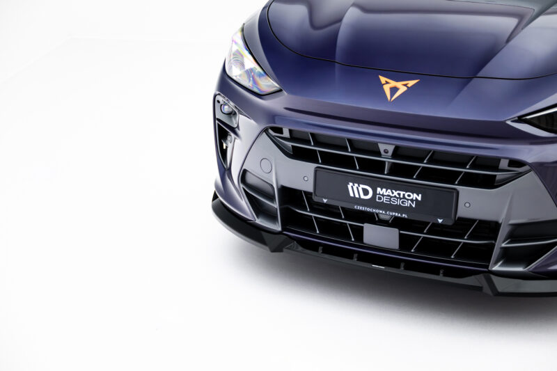 Close-up of a dark blue car's front end, featuring a headlight, glossy hood, and orange emblem on the hood.
