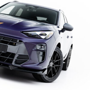 Close-up of the front-left of a purple SUV, showing the headlight, grille, and orange emblem on the hood.