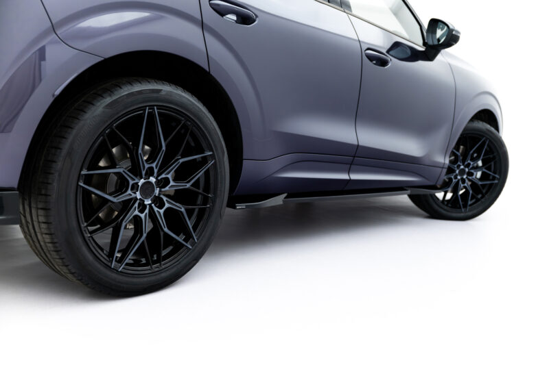 Close-up side view of a gray car highlighting a large black alloy wheel and tire near the front fender.