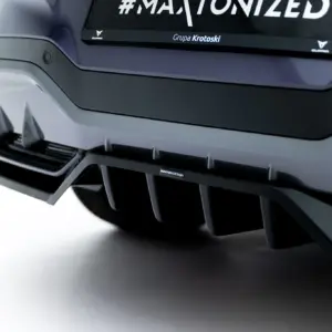 Close-up of a car front bumper with a dark grille and a small badge reading Grupa Krotoski on the bumper edge of a metallic vehicle surface