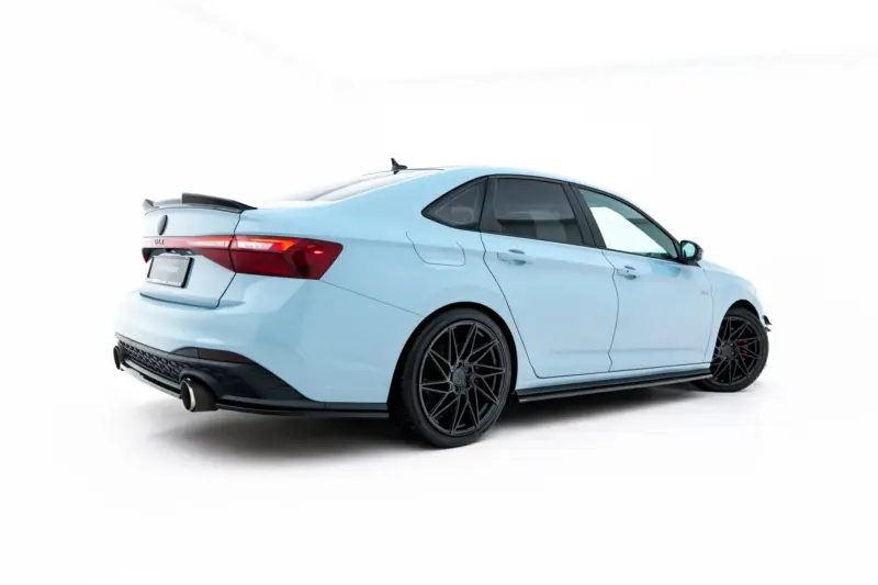 Rear three-quarter view of a light-blue sports sedan with a rear spoiler, black multi-spoke wheels, and red taillights in a white studio setting.