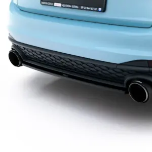 Close-up of a blue car's rear bumper with dual round exhausts and a black honeycomb grille, photographed against a white background.