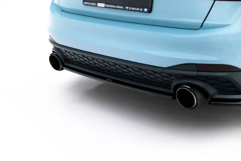 Close-up of a blue car's rear bumper with dual round exhausts and a black honeycomb grille, photographed against a white background.