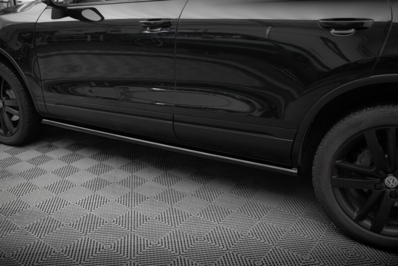 Close-up of a glossy black car door and front wheel on a textured showroom floor.