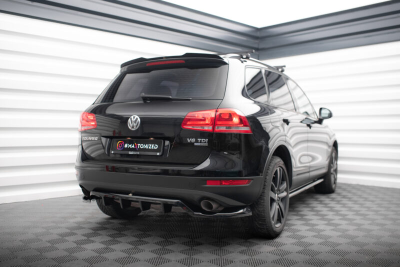 Rear three-quarter view of a black Volkswagen Touareg V6 TDI SUV in an indoor showroom, taillights on and glossy finish visible.
