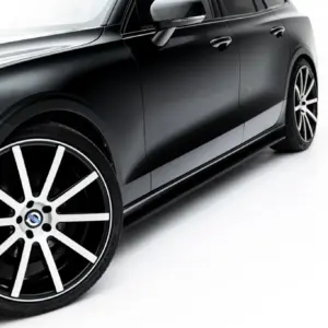 Close-up of a black car's side, showing the front wheel and sleek door with chrome mirror against a white background, angled view.