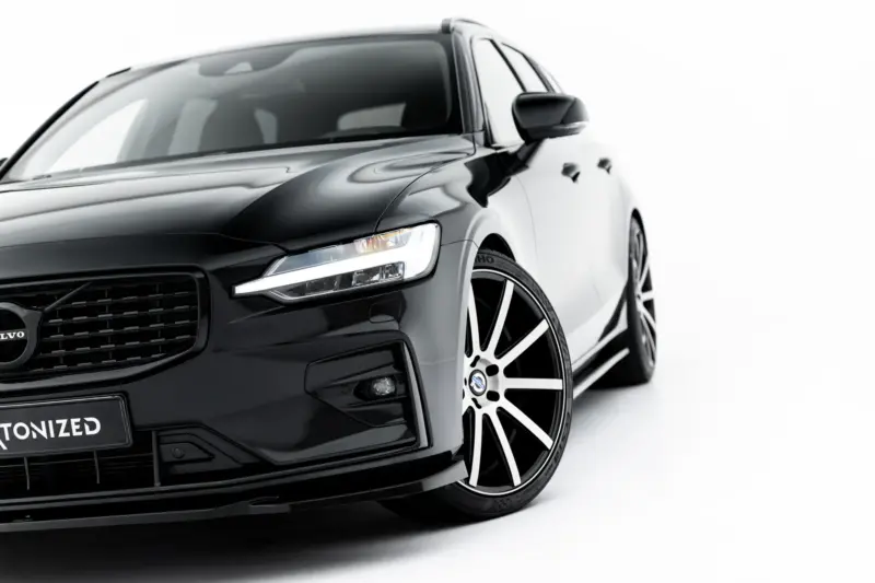 pol_po_Set-of-Splitters-Volvo-V60-R-Design-Mk3-23996_16webp - OPSHOLDERS Front-left quarter view of a glossy black Volvo car with a prominent grille, LED headlight, and large multi-spoke alloy wheel against a white background.