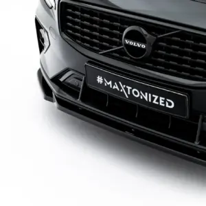 Close-up of a black Volvo car front, showing the grille, emblem, and a license plate reading #MAXTONIZED.