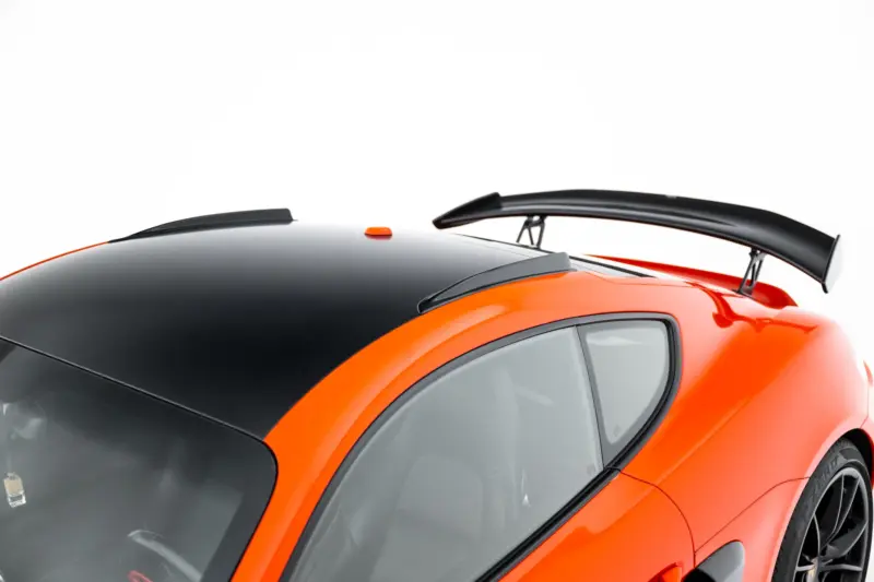 Close-up of an orange sports car roof with a black panoramic section and a large rear wing/spoiler above the rear window.