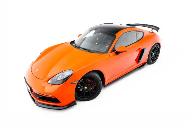 Bright orange Porsche sports car viewed from an elevated front-left angle, with a black roof and large rear spoiler.