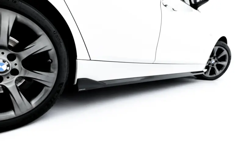 Close-up of a white BMW car’s front wheel and lower body panel, showing alloy wheel and tire detail.