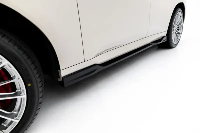 Close-up of a white car's side panel and alloy wheel, showing the lower body and wheel arch.