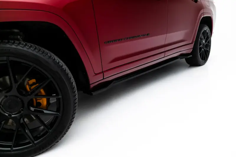 Close-up of a red Jeep Grand Cherokee side panel, showing the Grand Cherokee badge and a black alloy wheel with a yellow brake caliper.