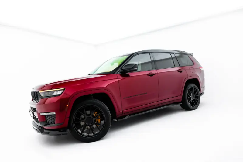 Red Jeep Grand Cherokee SUV photographed in a bright white studio with a low, front-left angle view and large black wheels.