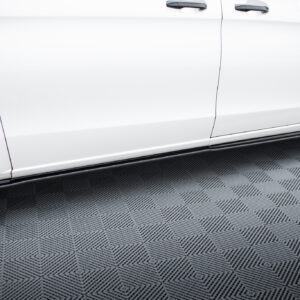 Close-up side view of a white car showing two doors, door handles, wheels, and a running board on a patterned floor.