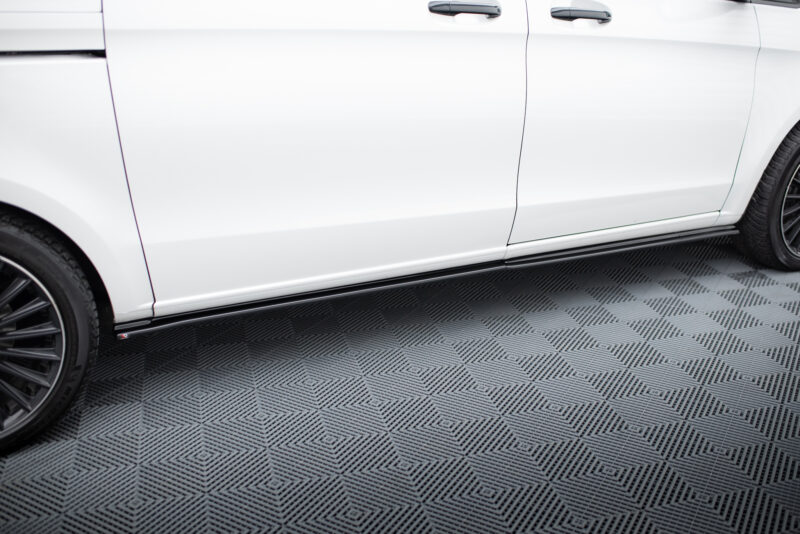 Close-up side view of a white car showing two doors, door handles, wheels, and a running board on a patterned floor.