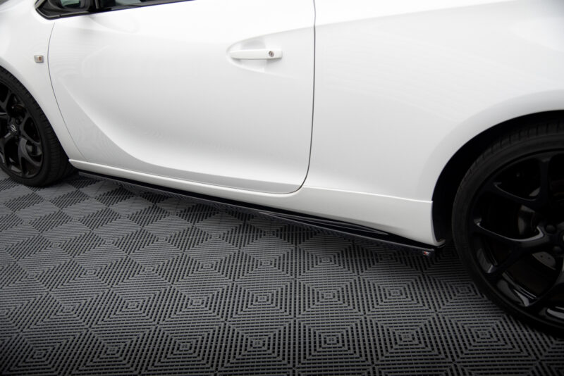 Close-up of a white car's side door, handle visible, with a black wheel and textured showroom floor beneath.