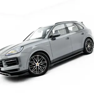 Side-front view of a silver Porsche SUV in a white studio setting, showing large alloy wheels and the hybrid badge.