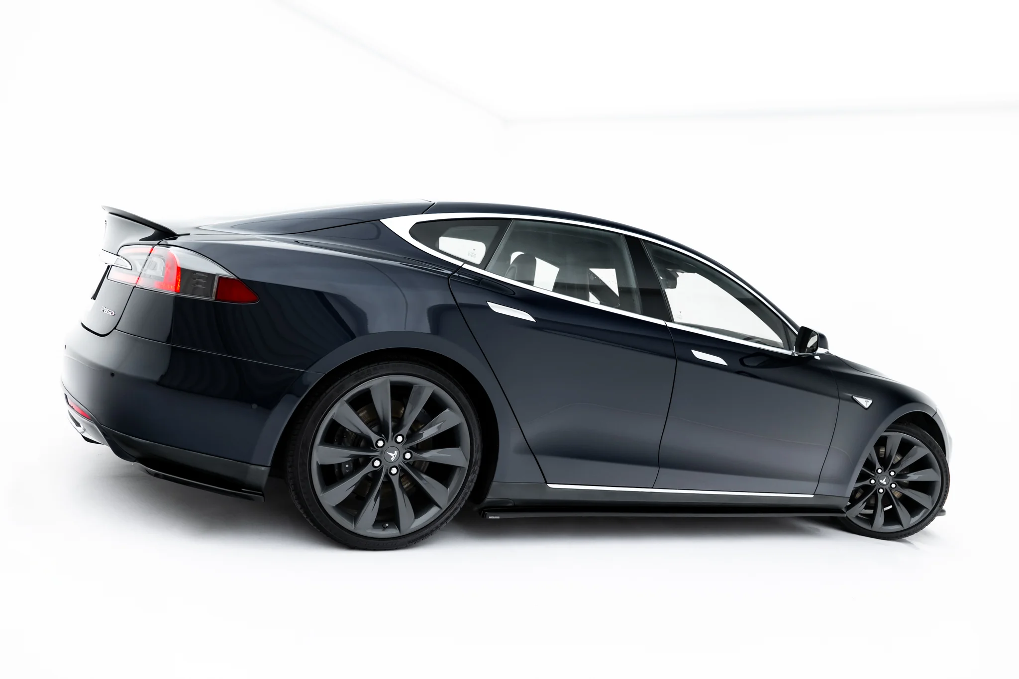 pol_po_Side-Skirts-Diffusers-V-1-Tesla-Model-S-Mk1-23946_6webp - OPSHOLDERS Partial side view of a dark blue Tesla Model S with large alloy wheels visible on a white background.