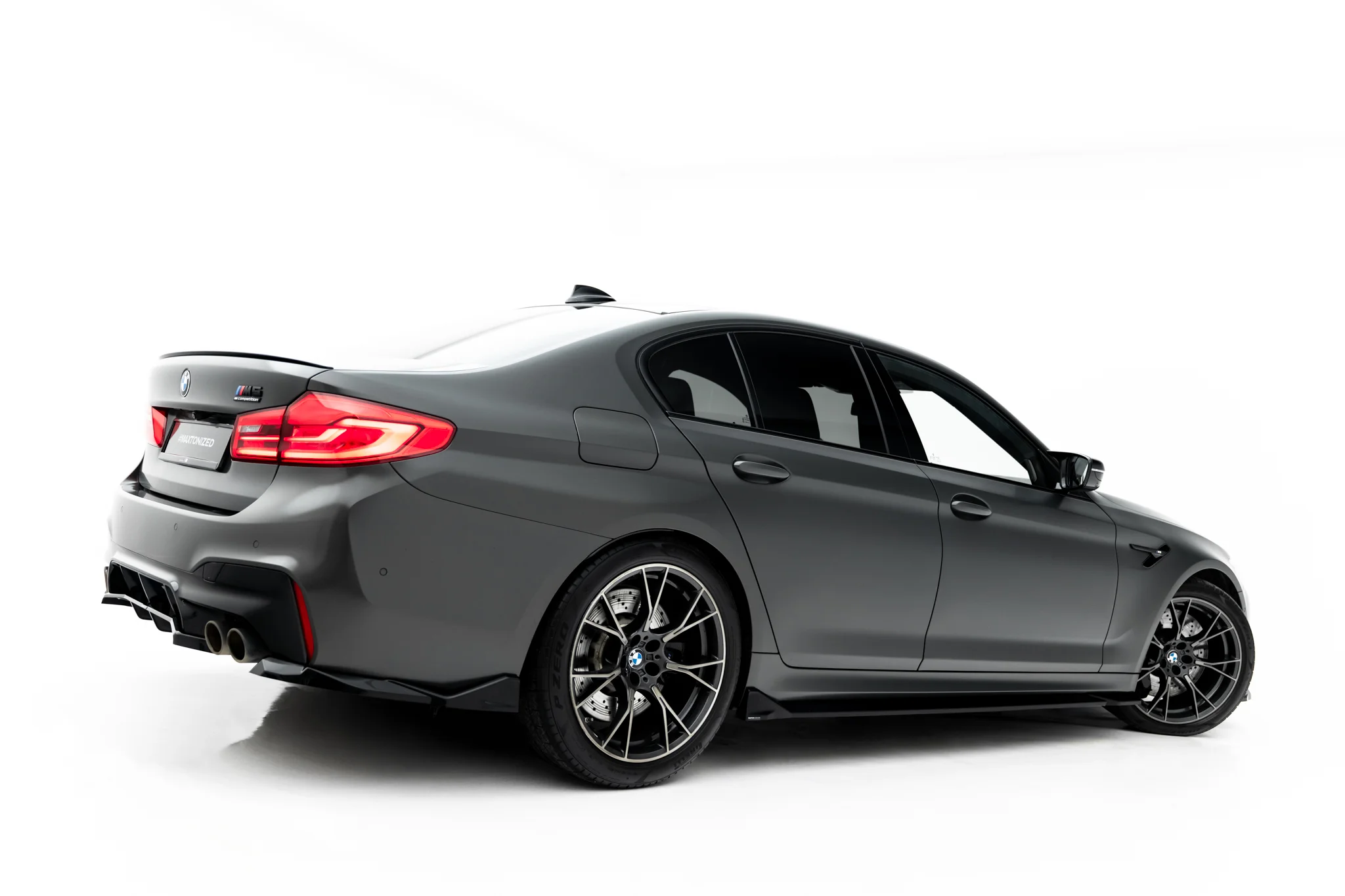 pol_po_Side-Skirts-Diffusers-V-2-BMW-M5-F90-23921_4webp - OPSHOLDERS Rear three-quarter view of a dark gray BMW M4 with quad exhausts and sporty alloy wheels, shown on a white studio background.