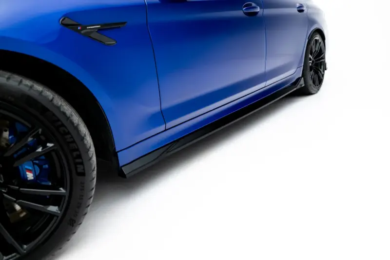 Close-up of a blue sports car's side panel, wheel and low side skirt, with an M badge on the vent.
