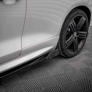 Close-up of a silver car's rear fender and black alloy wheel on a patterned metal floor, emphasizing wheel and body contour in a showroom setting.
