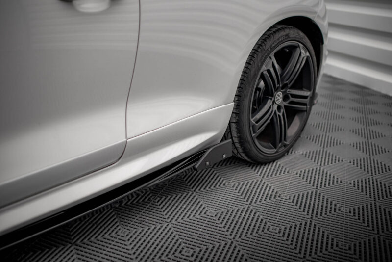 Close-up of a silver car's rear fender and black alloy wheel on a patterned metal floor, emphasizing wheel and body contour in a showroom setting.