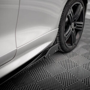 Close-up of a silver car’s side panel with a black alloy wheel and tire, shown against a patterned showroom floor.