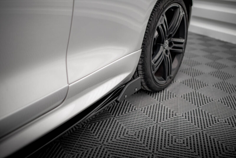 Close-up of a silver car’s side panel with a black alloy wheel and tire, shown against a patterned showroom floor.