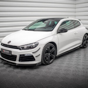 White two-door sports car parked indoors in front of a light gray, corrugated wall and checkered metal floor; visible VW badge on the hood.