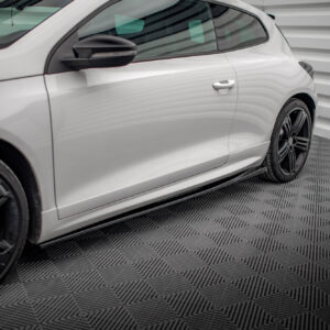 White car side view showing door, handle, and black alloy wheel against a ribbed background wall.