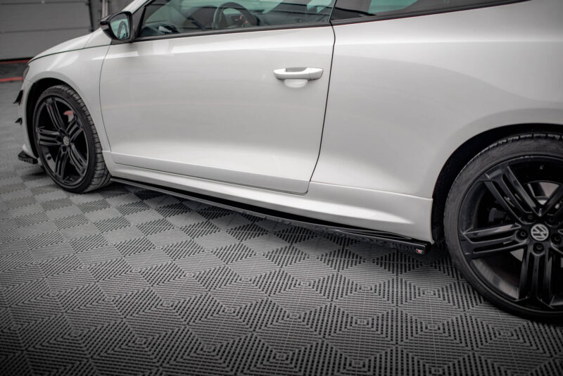 Side view of a white car showing the door and black alloy wheel on a patterned floor.