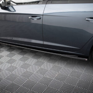 Close-up of a gray car's side with two doors, chrome handles, a side mirror, and alloy wheels on a patterned floor.