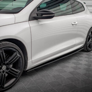 Close-up side view of a white car showing the driver-side door, black side mirror, and front wheel on a patterned floor.