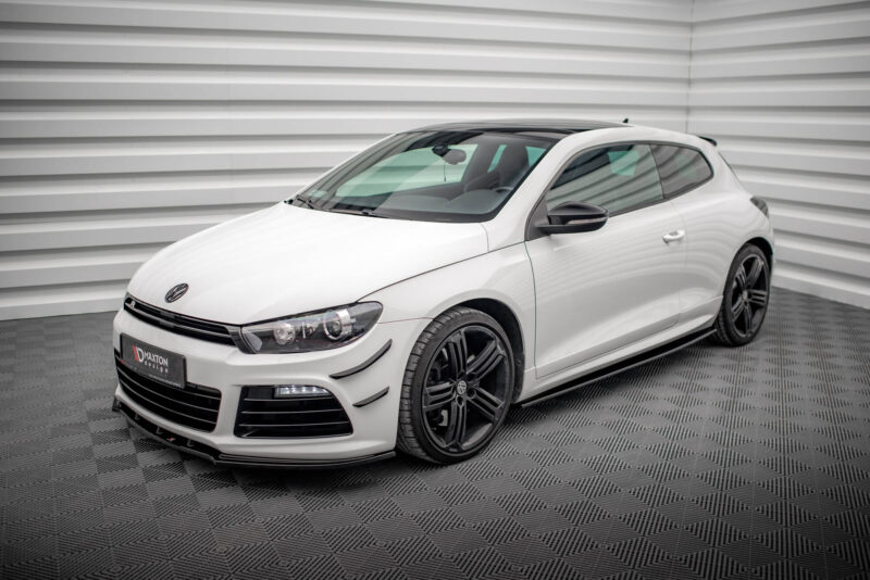 Front three-quarter view of a white Volkswagen sports hatchback in a showroom with a gray striped wall behind it with black alloy wheels visible on the right.