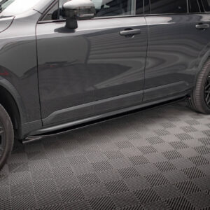 Close-up of a dark gray SUV's side, showing the doors, handles, and large black alloy wheels in a showroom setting by a patterned floor.