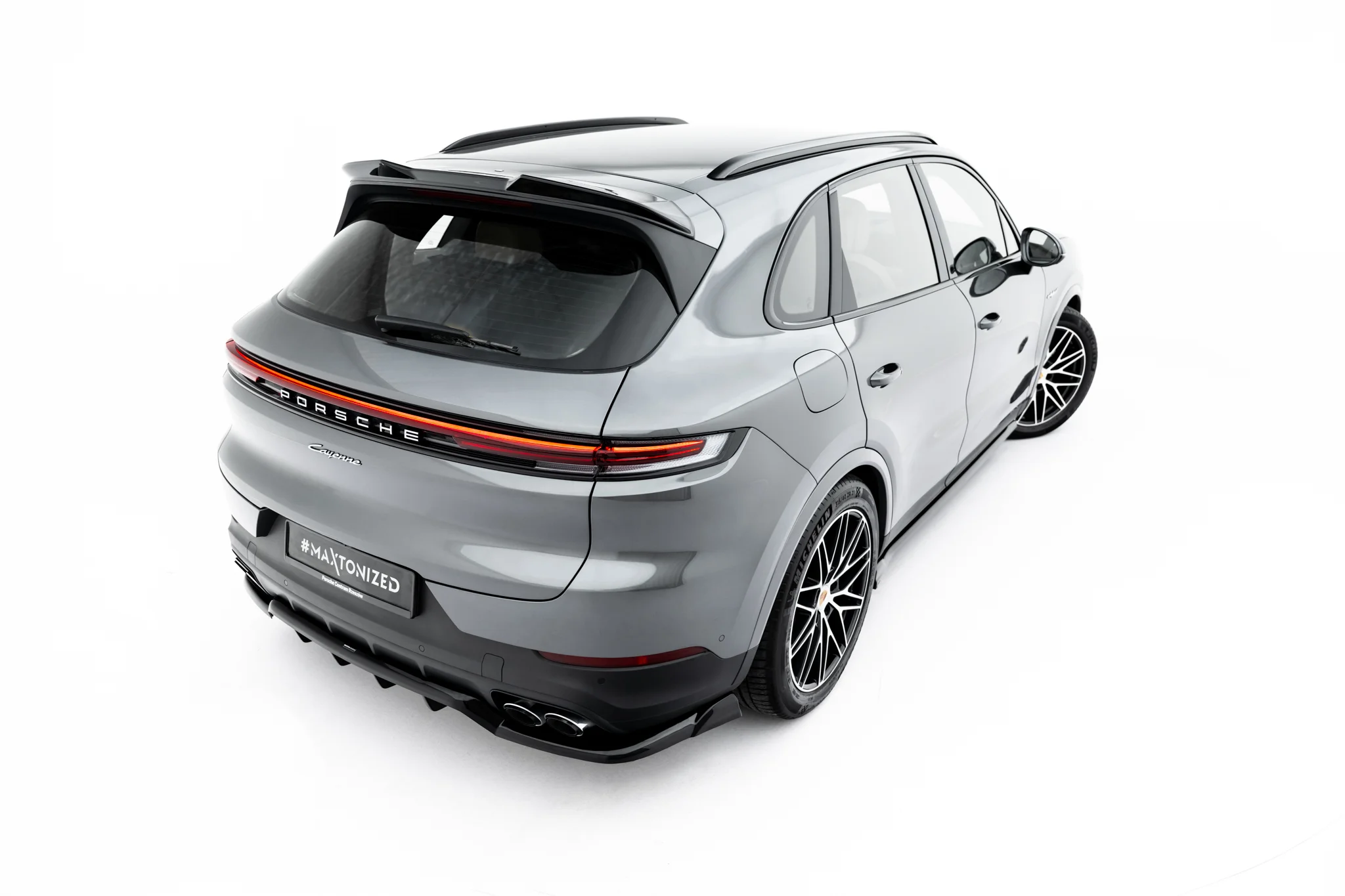 pol_po_Spoiler-Cap-3D-Porsche-Cayenne-SUV-Mk3-Facelift-23885_4webp - OPSHOLDERS Rear three-quarter view of a silver Porsche Cayenne SUV with black roof rails and stylish alloy wheels on a white background.